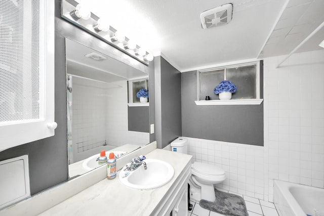 full bathroom featuring tile walls, tile patterned flooring, tiled shower / bath combo, vanity, and toilet