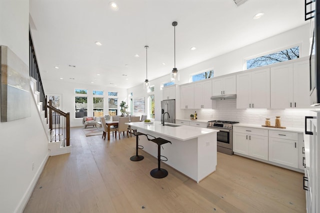 kitchen featuring a center island with sink, appliances with stainless steel finishes, decorative light fixtures, light countertops, and under cabinet range hood