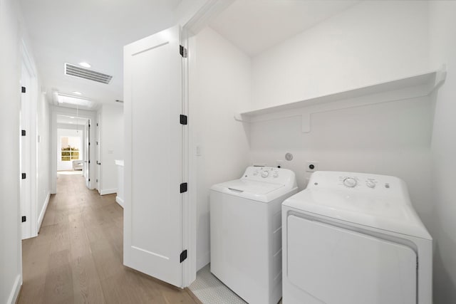 clothes washing area featuring washing machine and clothes dryer, visible vents, attic access, light wood-style floors, and laundry area