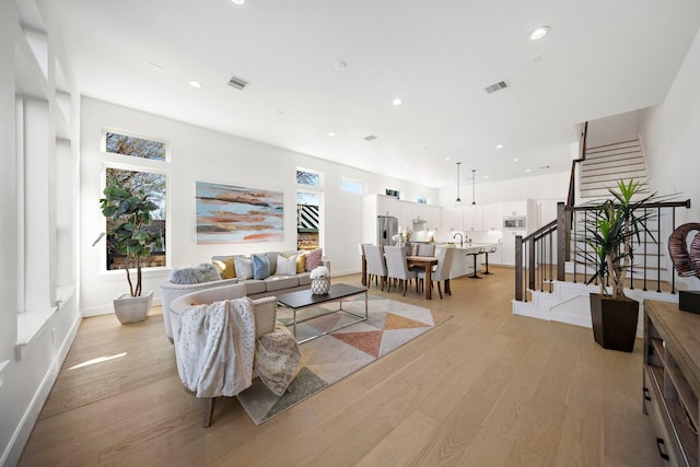 living area with light wood-style floors, recessed lighting, visible vents, and stairs