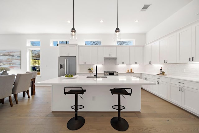 kitchen with pendant lighting, white cabinetry, sink, high end refrigerator, and a center island with sink