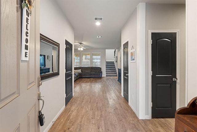 hallway with stairs, light wood-style flooring, baseboards, and visible vents