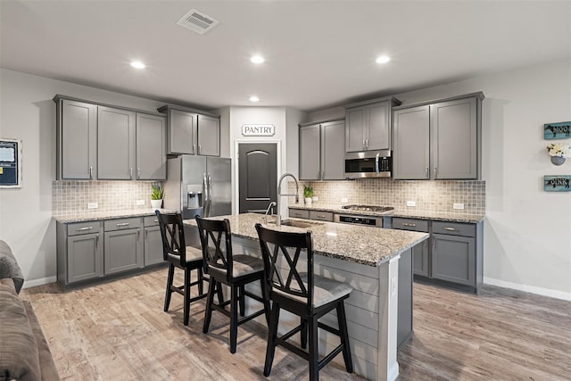 kitchen featuring a center island with sink, visible vents, gray cabinets, stainless steel appliances, and a kitchen bar