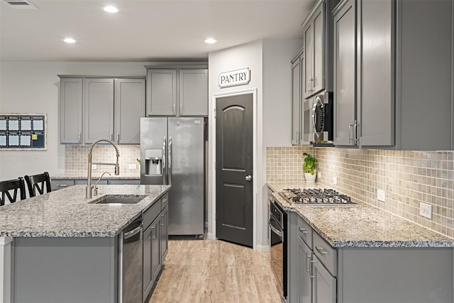 kitchen featuring stainless steel appliances, gray cabinets, a sink, and a center island with sink