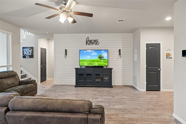 living room with light wood-type flooring, ceiling fan, visible vents, and baseboards