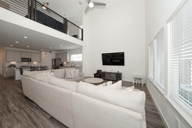 living room with dark wood-type flooring, ceiling fan, and a towering ceiling