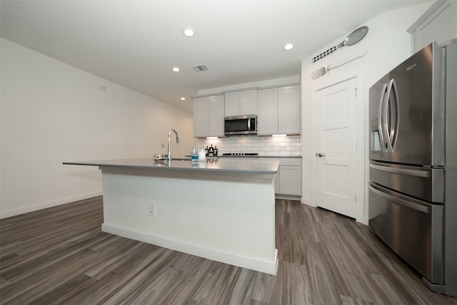 kitchen featuring appliances with stainless steel finishes, a kitchen island with sink, dark hardwood / wood-style floors, and decorative backsplash