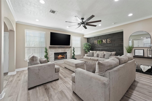 living room featuring ceiling fan, a fireplace, ornamental molding, and a textured ceiling