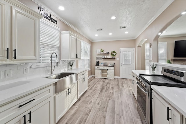 kitchen featuring sink, crown molding, white cabinetry, backsplash, and stainless steel electric range oven