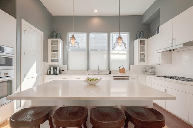 kitchen featuring sink, hanging light fixtures, appliances with stainless steel finishes, a kitchen breakfast bar, and white cabinets