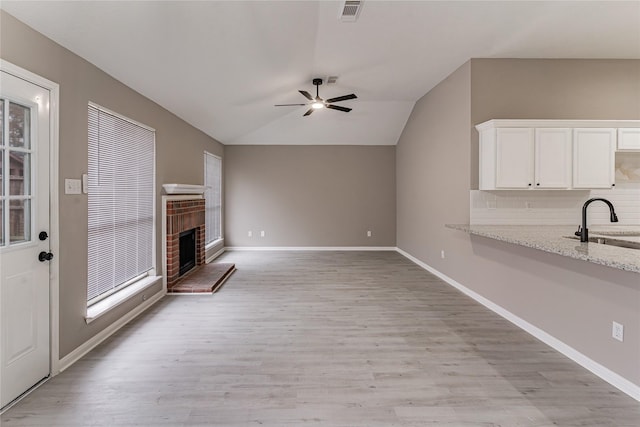 unfurnished living room with lofted ceiling, sink, ceiling fan, a fireplace, and light hardwood / wood-style floors