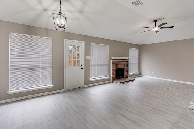 unfurnished living room featuring lofted ceiling, ceiling fan with notable chandelier, a fireplace, and light hardwood / wood-style flooring