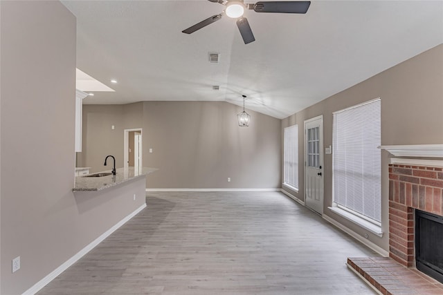 unfurnished living room featuring vaulted ceiling, a fireplace, sink, ceiling fan, and light hardwood / wood-style floors