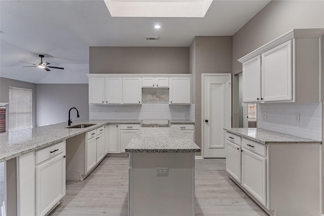 kitchen with white cabinetry, a center island, sink, and kitchen peninsula