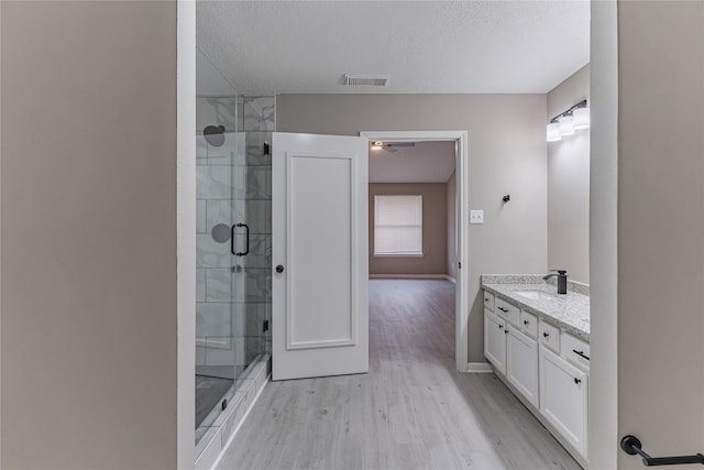 bathroom with vanity, wood-type flooring, an enclosed shower, and a textured ceiling