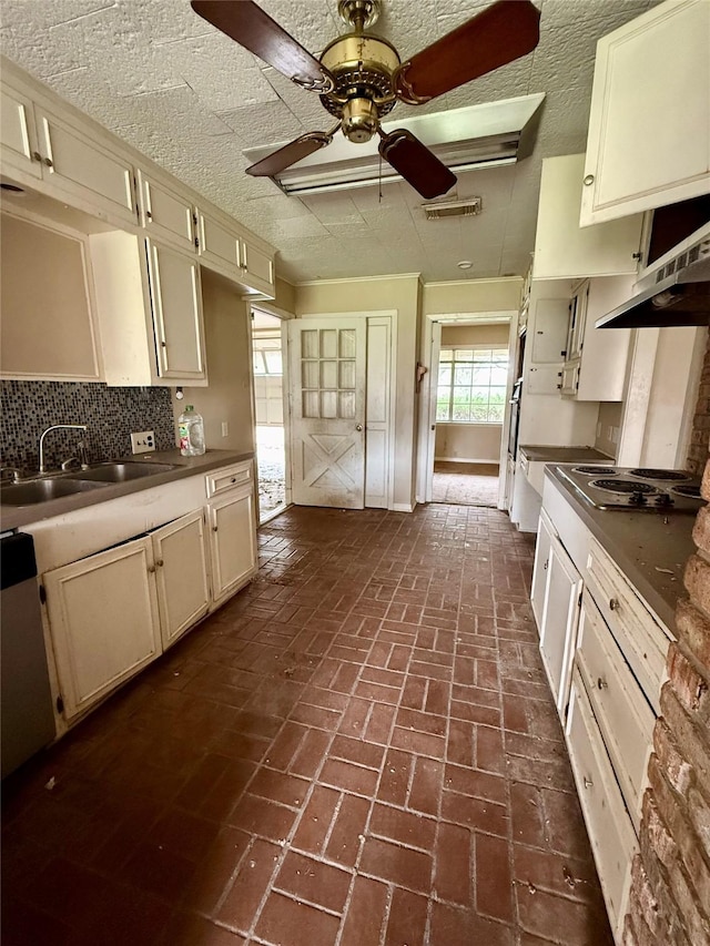 kitchen featuring decorative backsplash, a ceiling fan, a sink, brick floor, and stainless steel electric stovetop