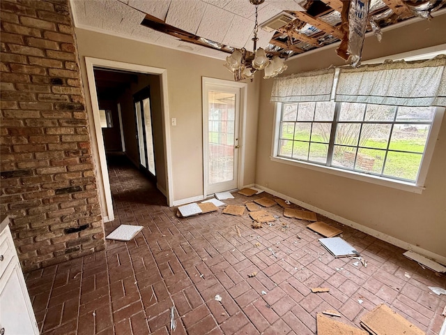 unfurnished dining area with an inviting chandelier, baseboards, brick floor, and a textured ceiling