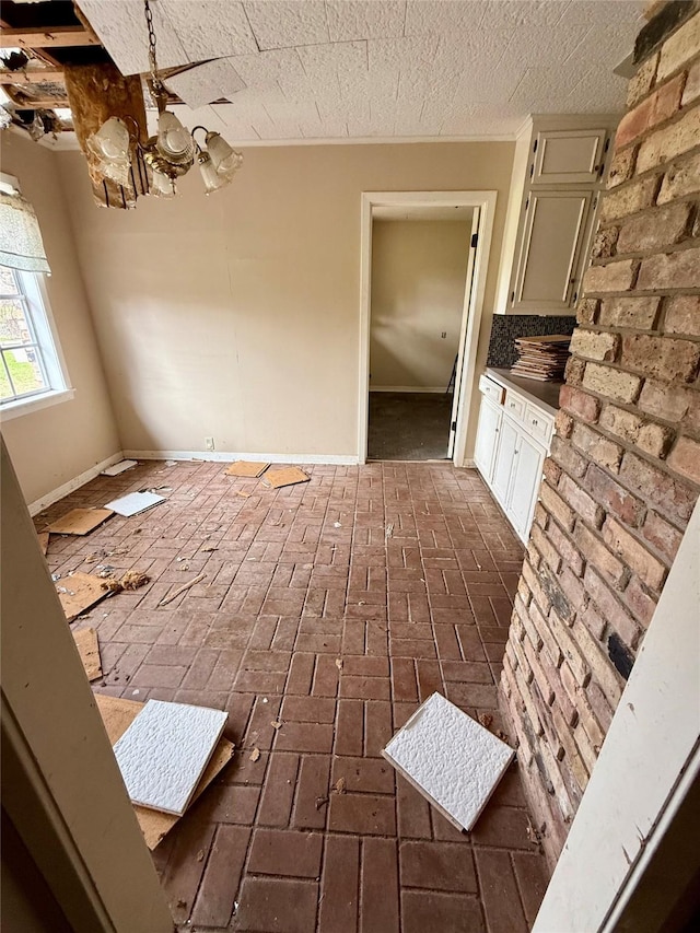 interior space featuring a notable chandelier, a textured ceiling, brick floor, and baseboards