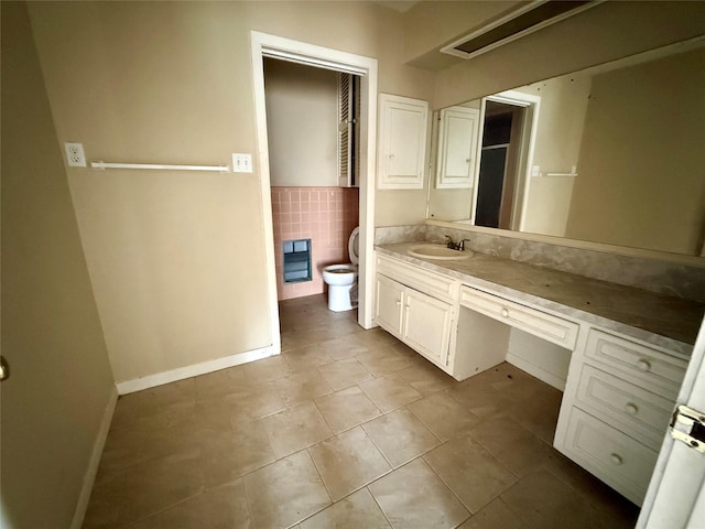 bathroom featuring toilet, vanity, baseboards, tile walls, and tile patterned floors