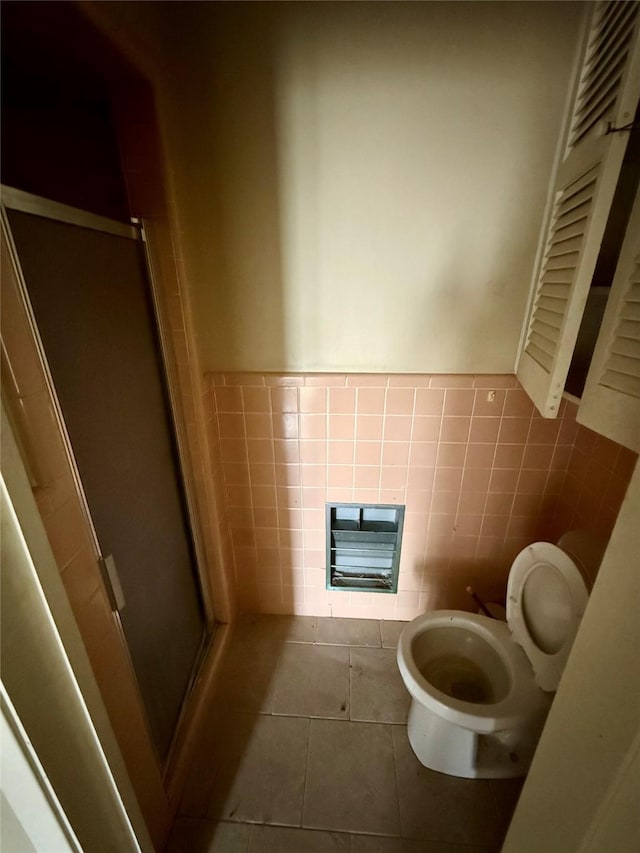 full bathroom with toilet, a stall shower, tile patterned flooring, and tile walls