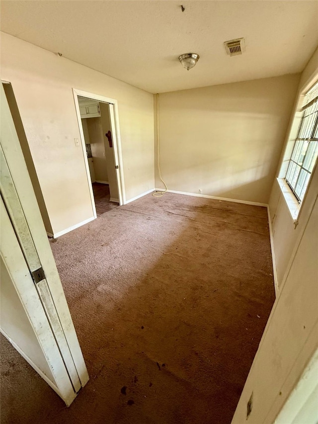 spare room featuring carpet floors, visible vents, and baseboards