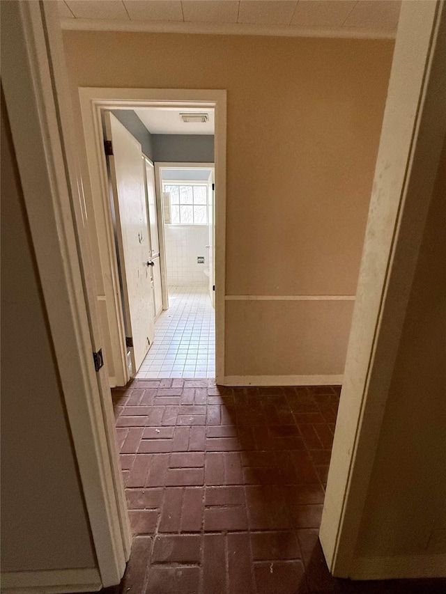 corridor featuring brick floor, visible vents, crown molding, and baseboards