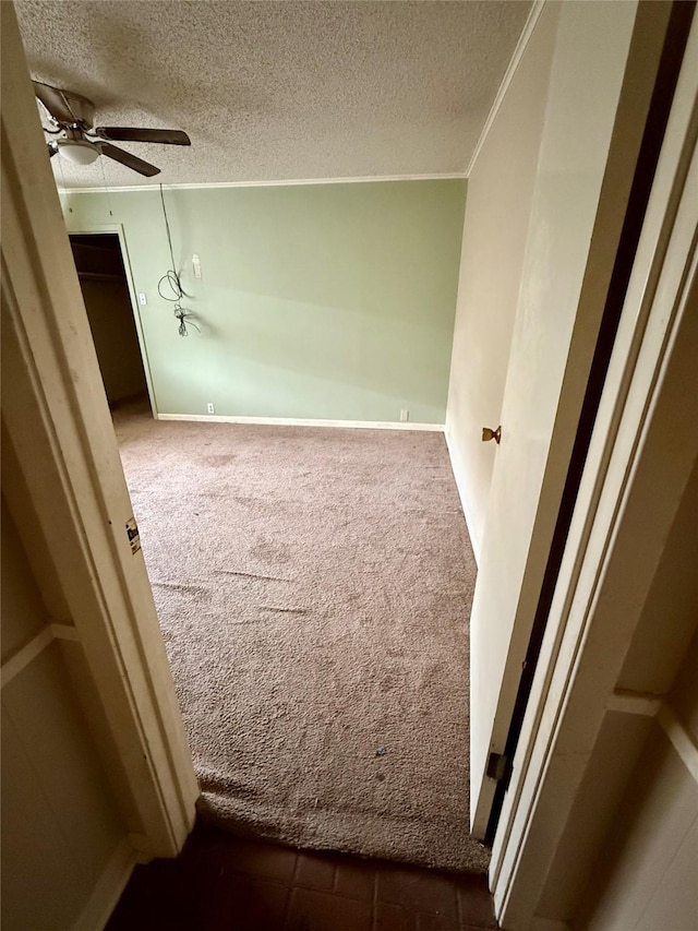 spare room featuring baseboards, a ceiling fan, dark colored carpet, crown molding, and a textured ceiling