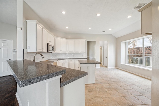 kitchen featuring vaulted ceiling, a breakfast bar, white cabinetry, decorative backsplash, and a center island