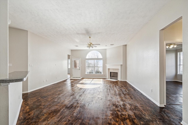 unfurnished living room featuring dark wood-type flooring, ceiling fan, and a textured ceiling