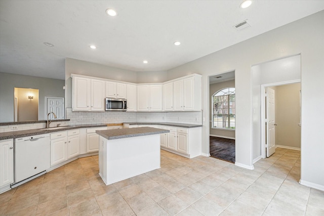 kitchen with white cabinetry, dishwasher, sink, decorative backsplash, and a center island