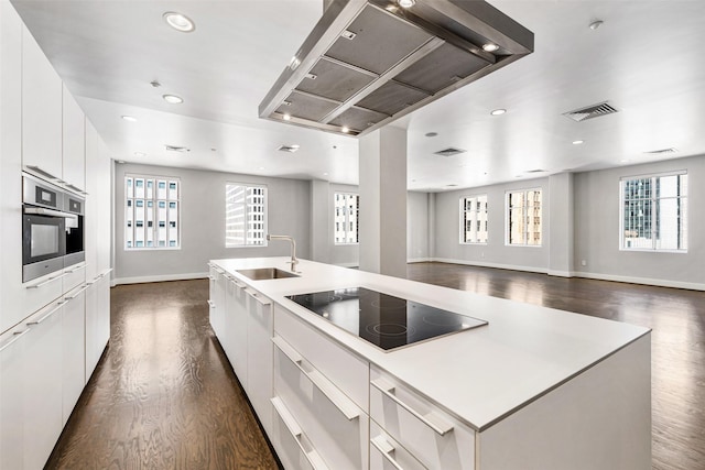 kitchen with sink, white cabinetry, black electric stovetop, a center island with sink, and stainless steel oven