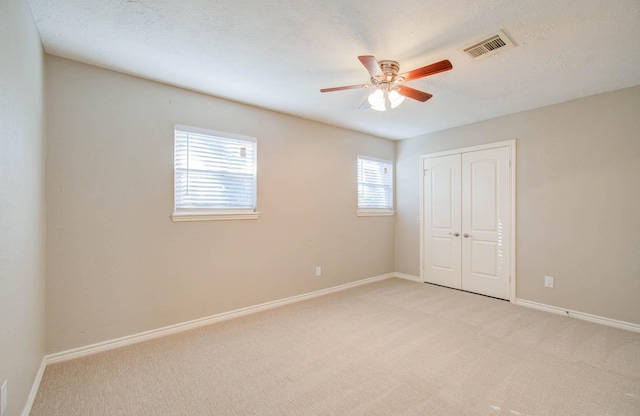 unfurnished bedroom featuring ceiling fan, a closet, light carpet, and a textured ceiling