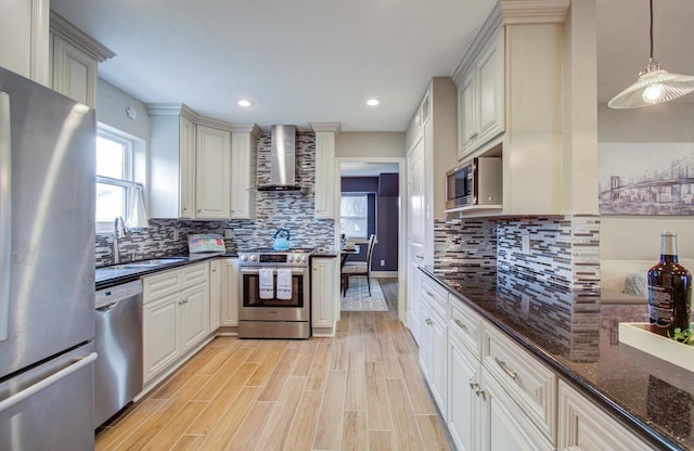 kitchen featuring pendant lighting, sink, dark stone counters, stainless steel appliances, and wall chimney exhaust hood