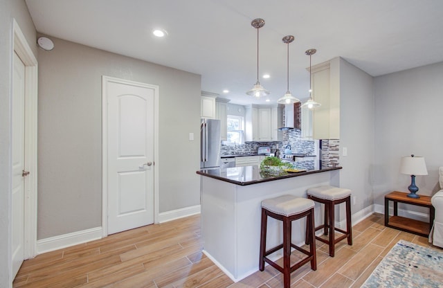 kitchen with decorative light fixtures, white cabinetry, a kitchen breakfast bar, kitchen peninsula, and wall chimney exhaust hood