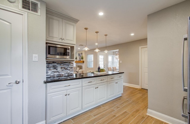 kitchen with stainless steel microwave, white cabinetry, pendant lighting, and decorative backsplash