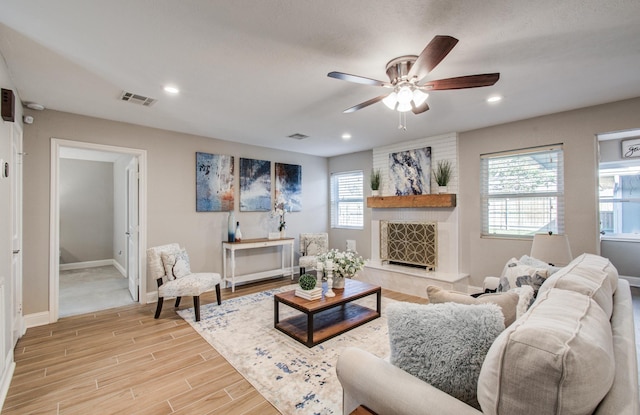 living room featuring light hardwood / wood-style flooring, a large fireplace, and ceiling fan