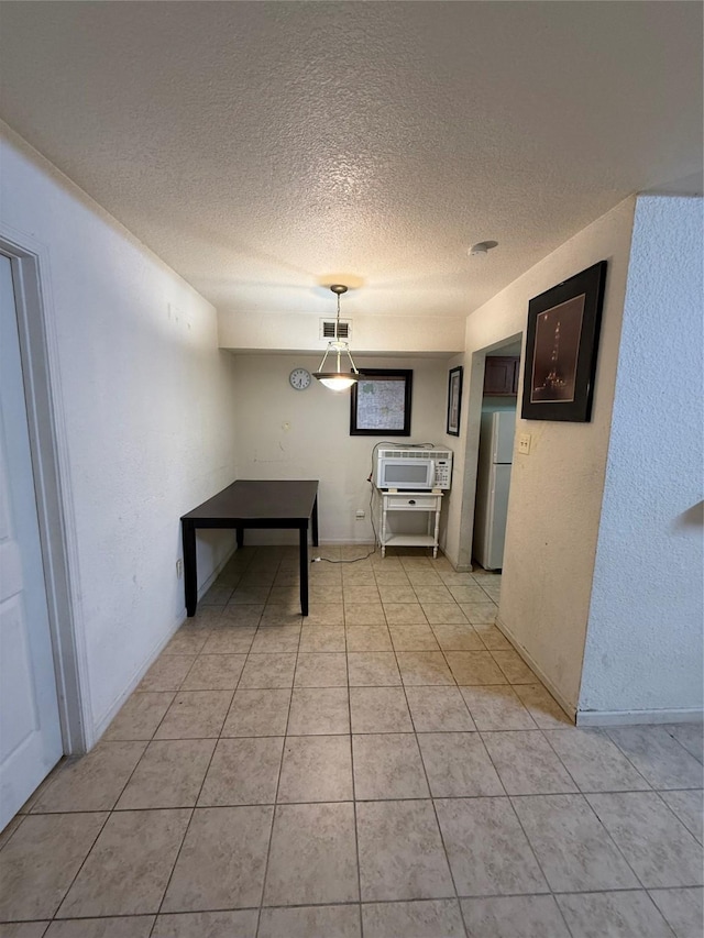 hall with a wall mounted air conditioner, a textured ceiling, and light tile patterned floors