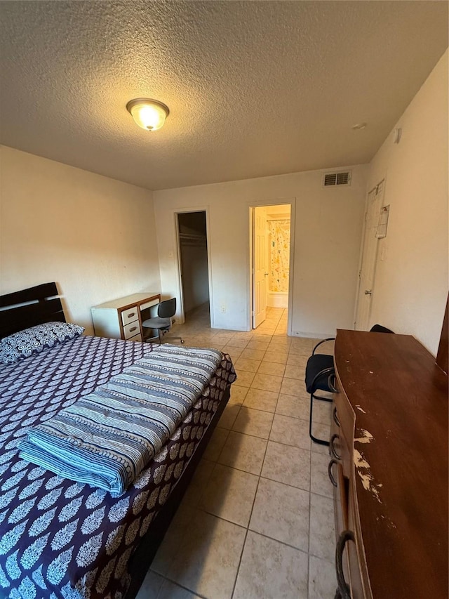 tiled bedroom with ensuite bathroom, a textured ceiling, and a closet