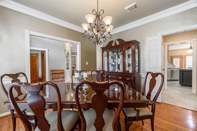 dining area with crown molding, light hardwood / wood-style floors, and a notable chandelier