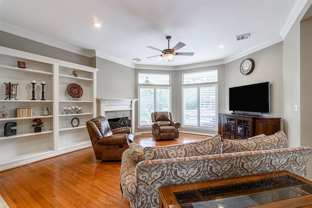 living room featuring hardwood / wood-style floors, ornamental molding, a tile fireplace, and ceiling fan