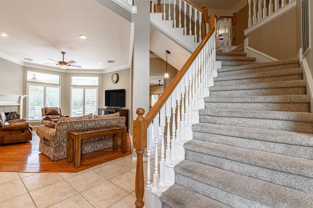 stairway with tile patterned flooring, a fireplace, ornamental molding, and ceiling fan