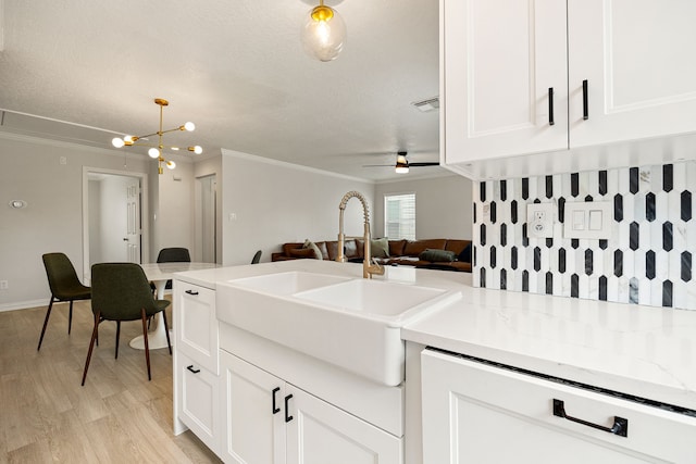 kitchen with ceiling fan with notable chandelier, white cabinetry, sink, ornamental molding, and light hardwood / wood-style flooring