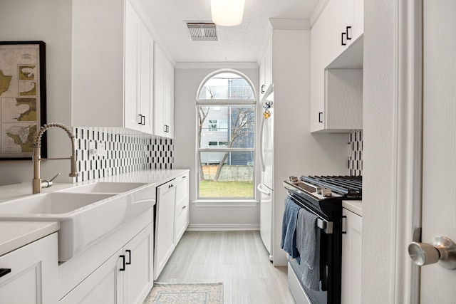 kitchen featuring sink, white cabinetry, crown molding, plenty of natural light, and stainless steel range with gas stovetop