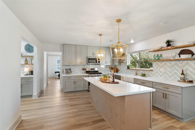 kitchen with gray cabinetry, stainless steel appliances, a center island, decorative light fixtures, and decorative backsplash