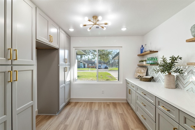 interior space with light wood-type flooring, an inviting chandelier, gray cabinetry, and decorative backsplash