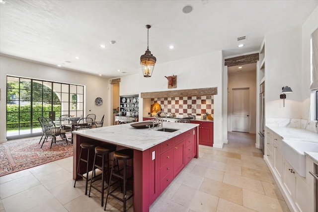 kitchen with tasteful backsplash, sink, light stone counters, and a center island with sink