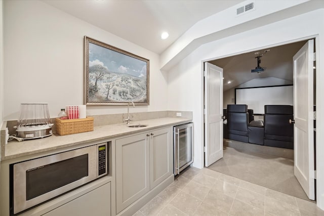 kitchen featuring sink, vaulted ceiling, light carpet, beverage cooler, and white cabinets