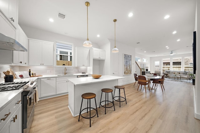 kitchen with sink, stainless steel gas stove, white cabinets, a kitchen island, and decorative light fixtures