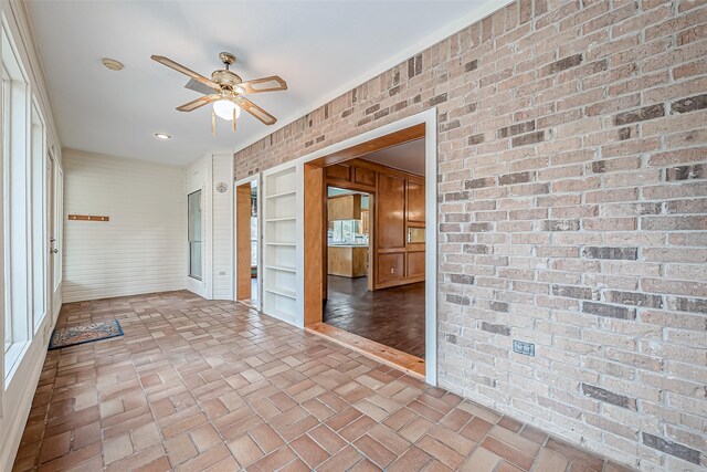 unfurnished room with ceiling fan and brick wall