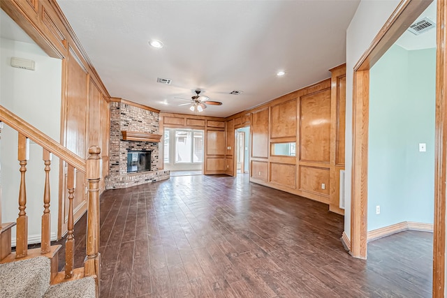 unfurnished living room featuring ornamental molding, wooden walls, dark hardwood / wood-style floors, ceiling fan, and a fireplace